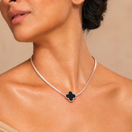 A close-up of a model wearing a delicate rose gold chain necklace with a black clover-shaped pendant.