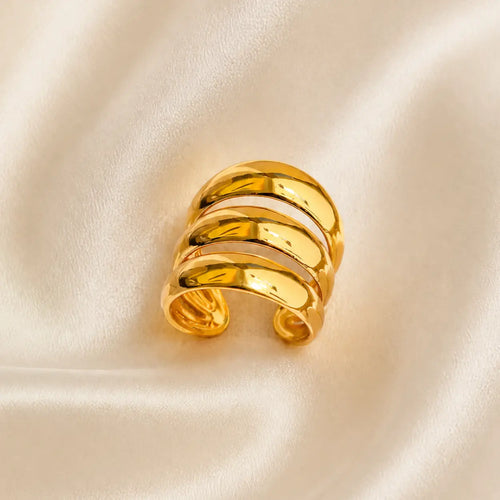 A polished gold wrap ring with three horizontal bands, displayed on a soft, cream-colored satin fabric background.