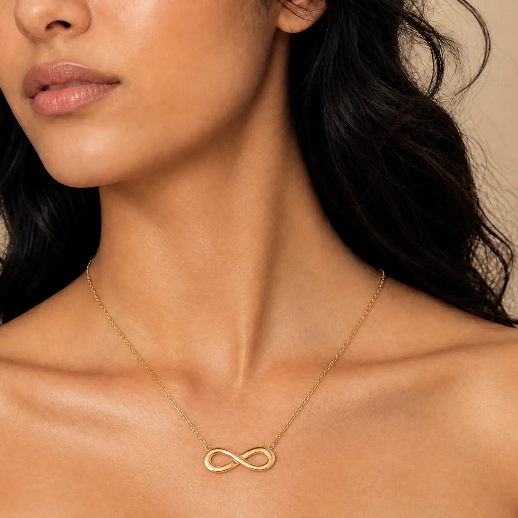 A close-up of a model wearing a delicate gold infinity necklace with a fine chain and a polished infinity symbol pendant.