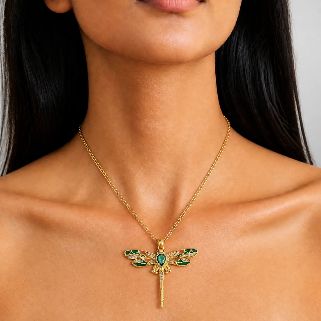 A gold dragonfly pendant necklace with green enamel details, worn by a model.
