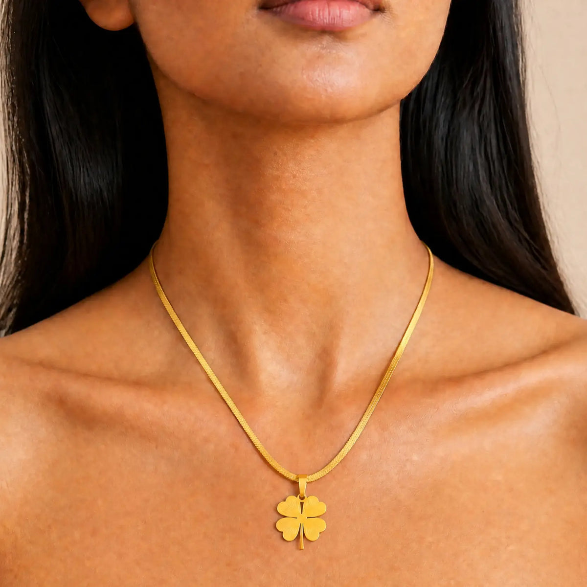 A close-up of a model wearing a delicate gold chain necklace with a small four-leaf clover pendant.