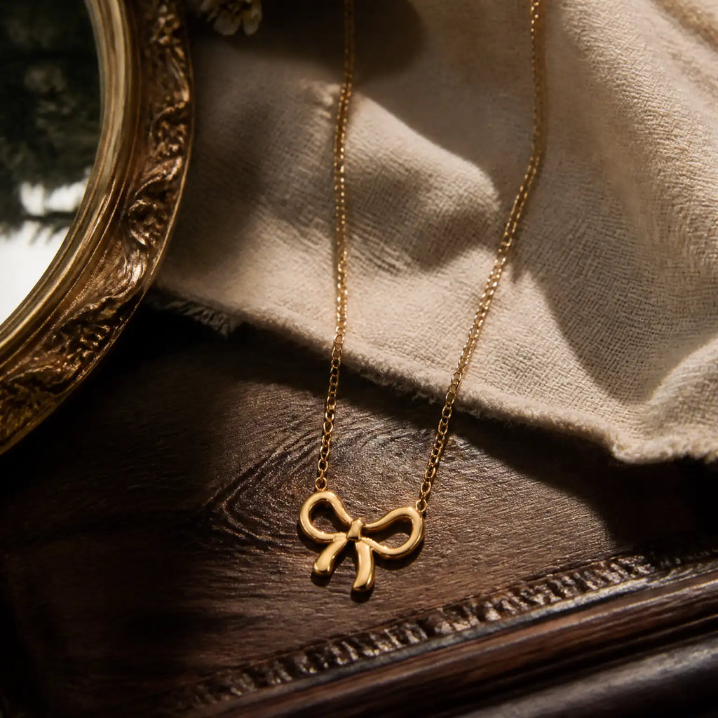 Anti-tarnish gold stainless steel chain necklace with a polished gold ribbon bow pendant.