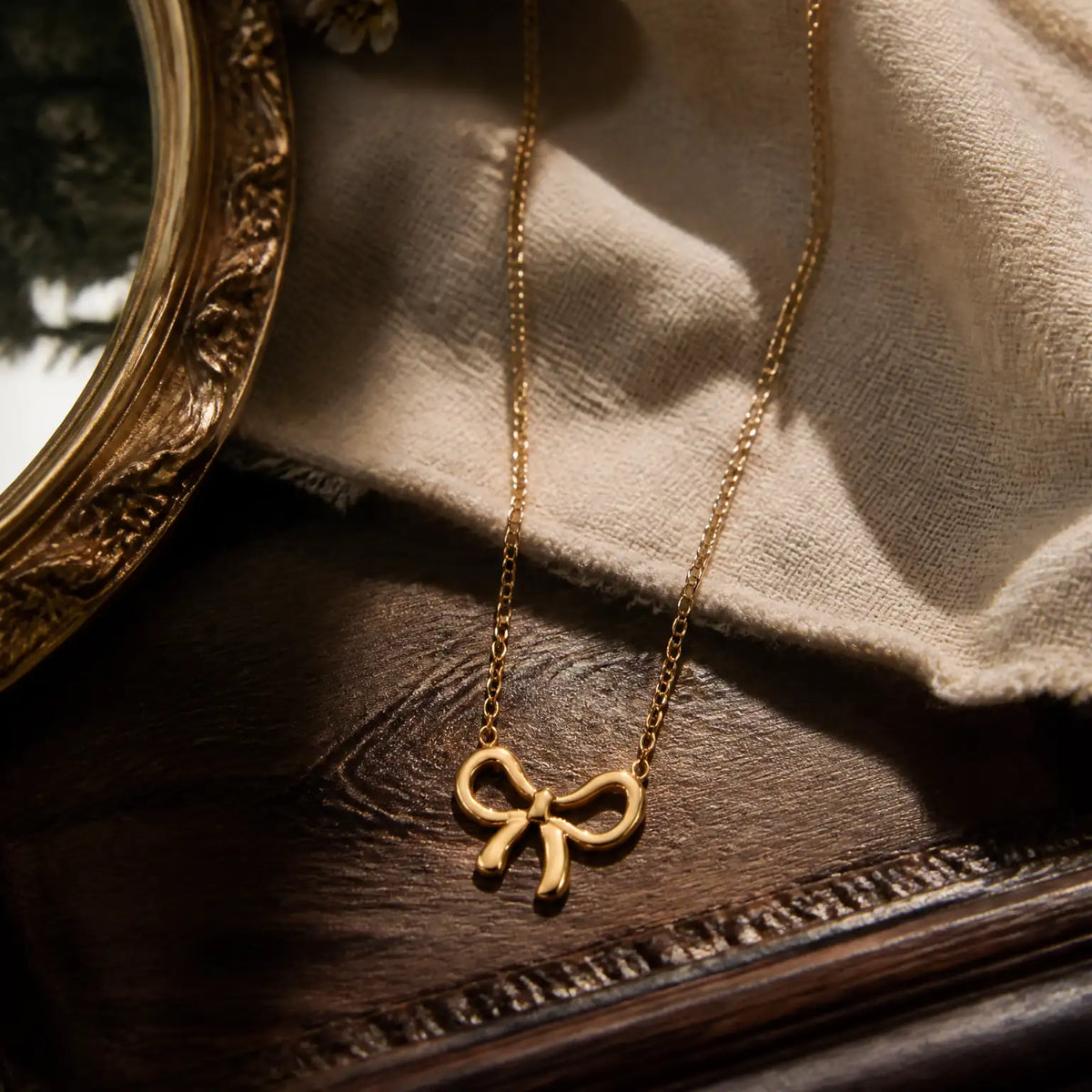 Anti-tarnish gold stainless steel chain necklace with a polished gold ribbon bow pendant.
