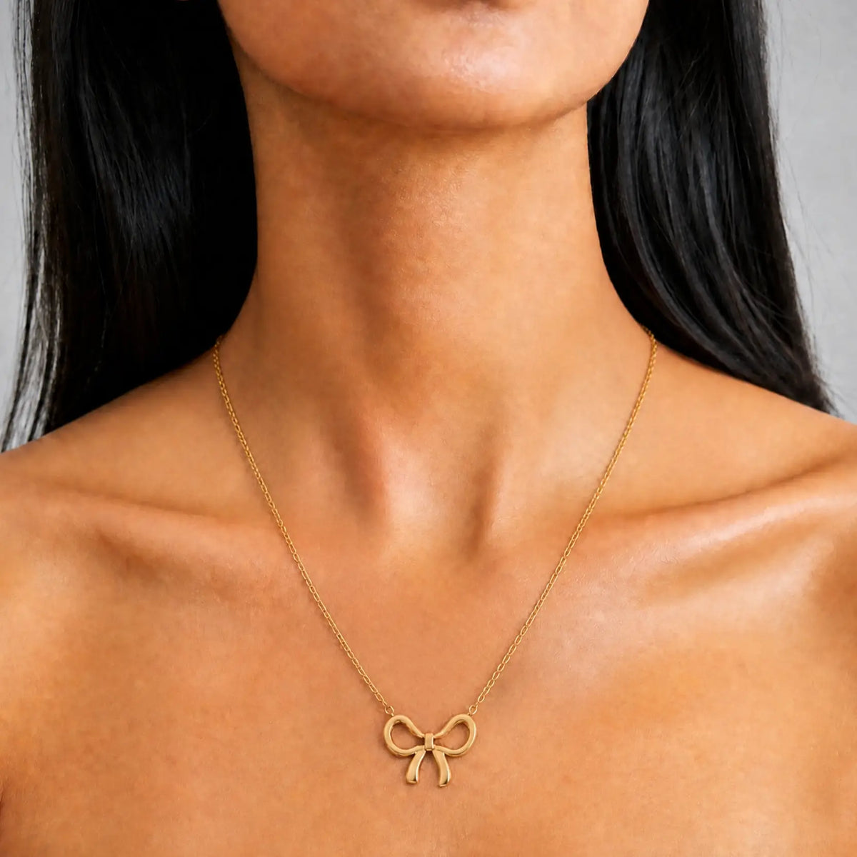 Anti-tarnish gold stainless steel chain necklace with a polished gold ribbon bow pendant.