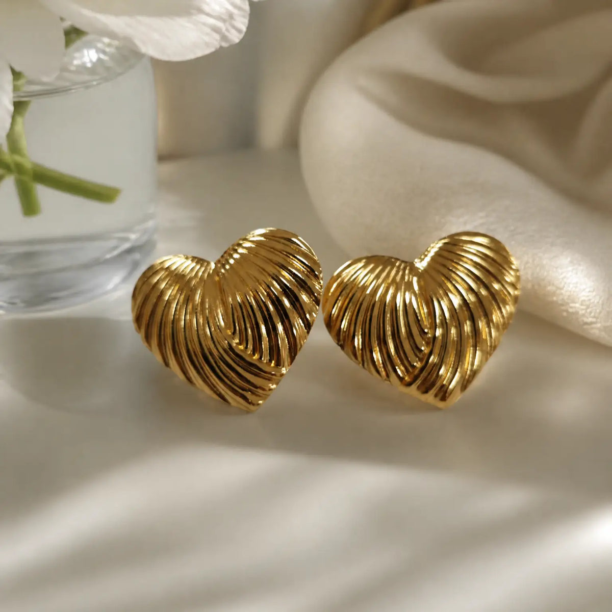 A pair of gold cufflinks shaped like a starfish and a spiral shell, displayed on a dark textured slate surface with scattered gold foil flakes.